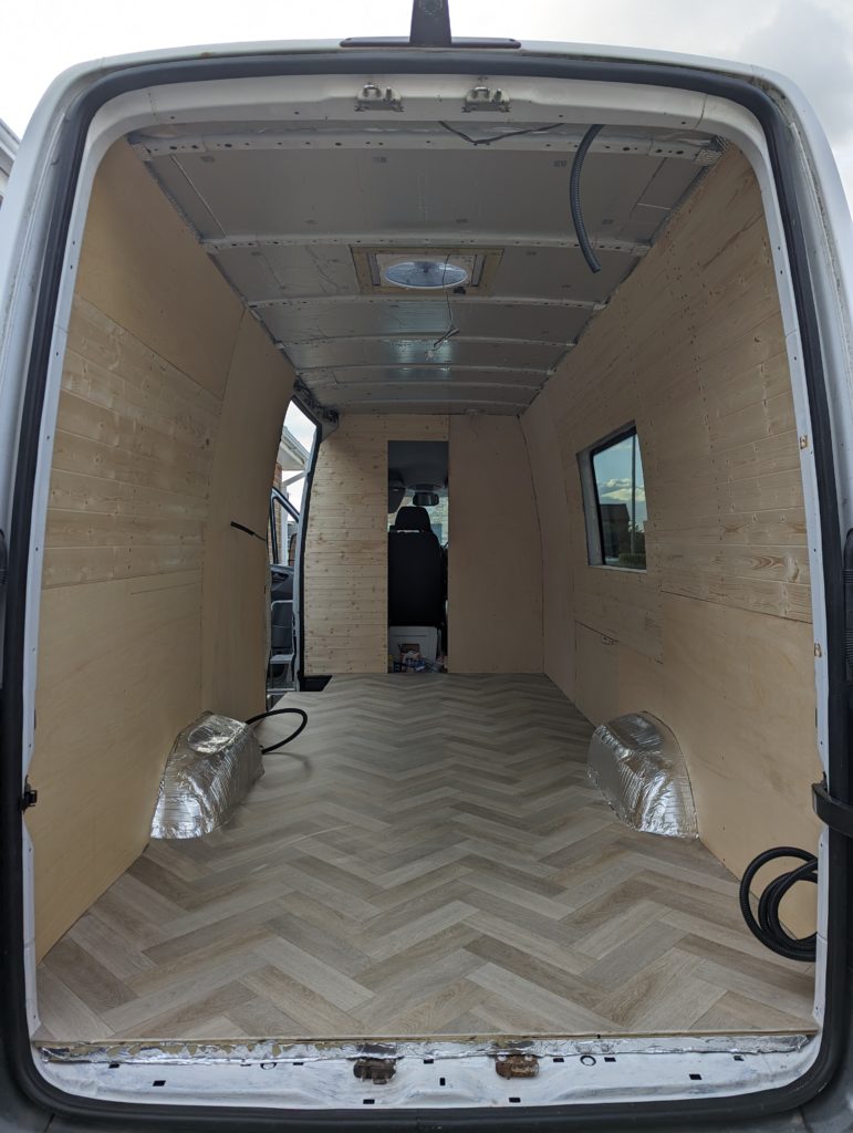 A picture of our campervan from the back, with neutral herringbone vinyl flooring, cladded walls and an insulated roof.