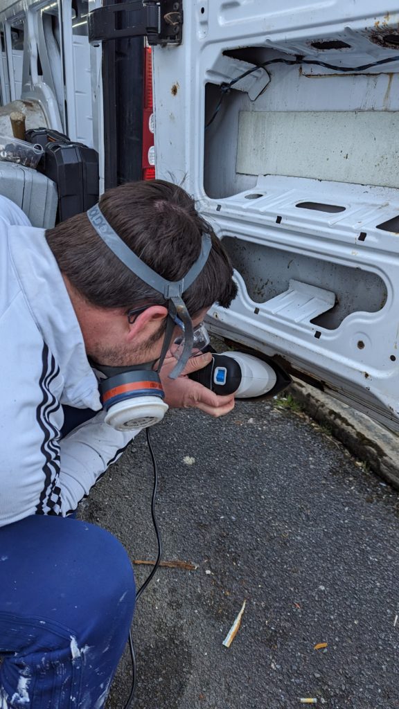 andrew sanding the back door of our sprinter van to remove loose rust