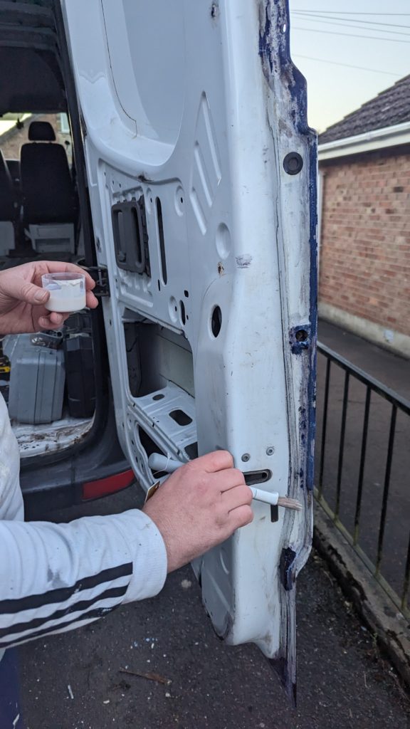 andrew applying rust converter on the back door of our sprinter to treat the rust