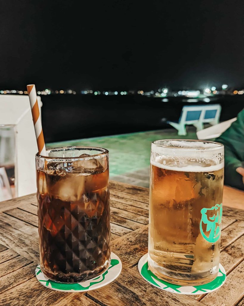 Two drinks - a coke & a beer sitting on a table at Uga Uga, Corralejo. Views over the waterfront.