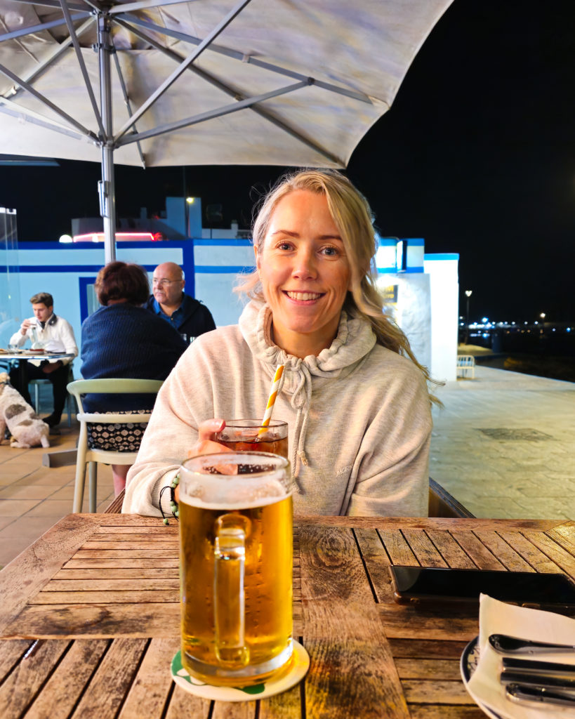 Jane sitting at UGA UGA Corralejo in her hoody, tired but enjoying her drink !