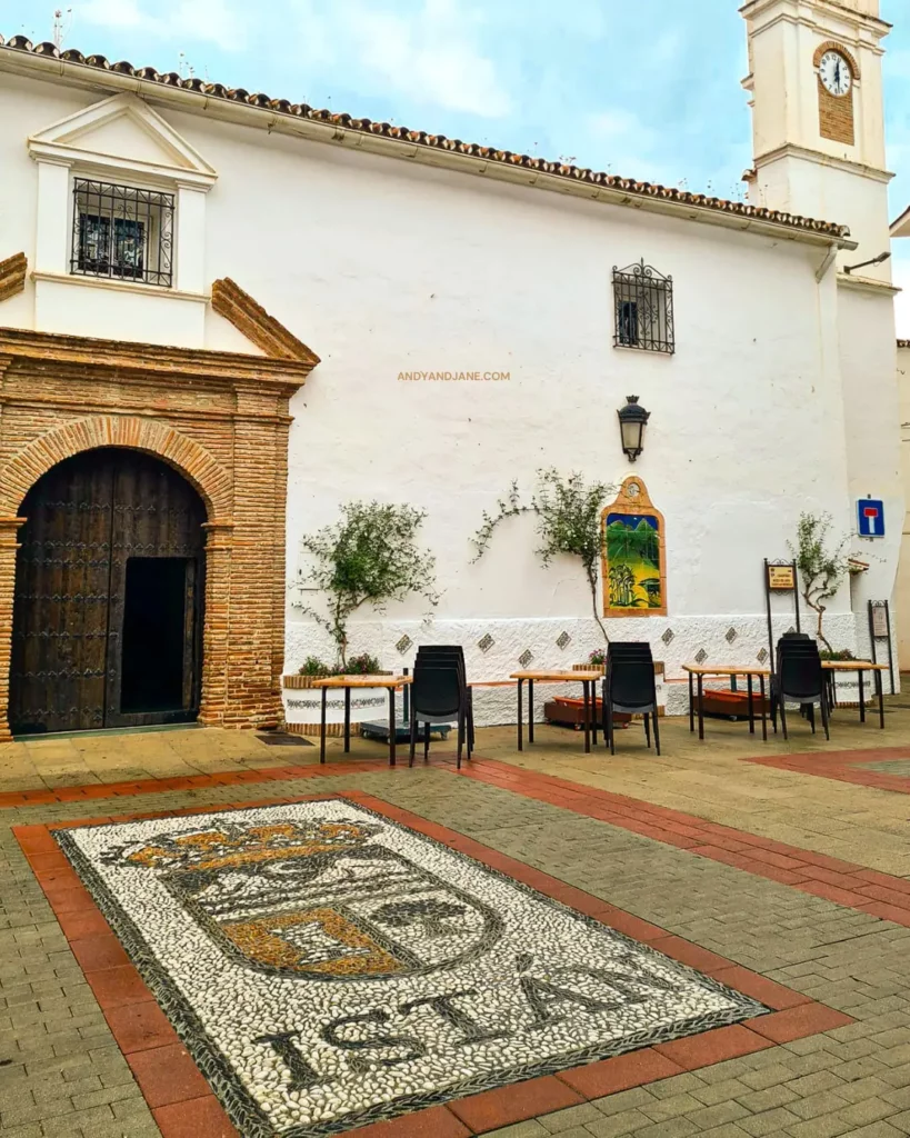 The front of a church in Istan with an old archway & brown door, with seats outside for locals to sit.