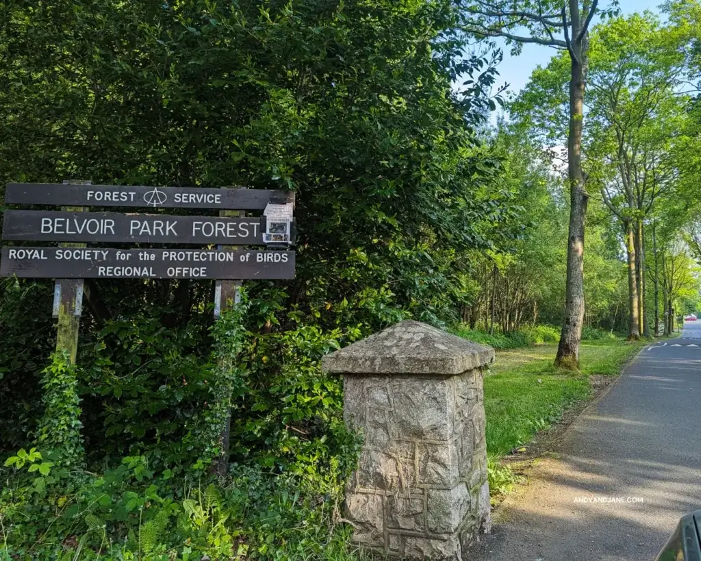 A sign reading "Belvoir Park Forest" stands against a backdrop of trees, indicating the entrance to the park.