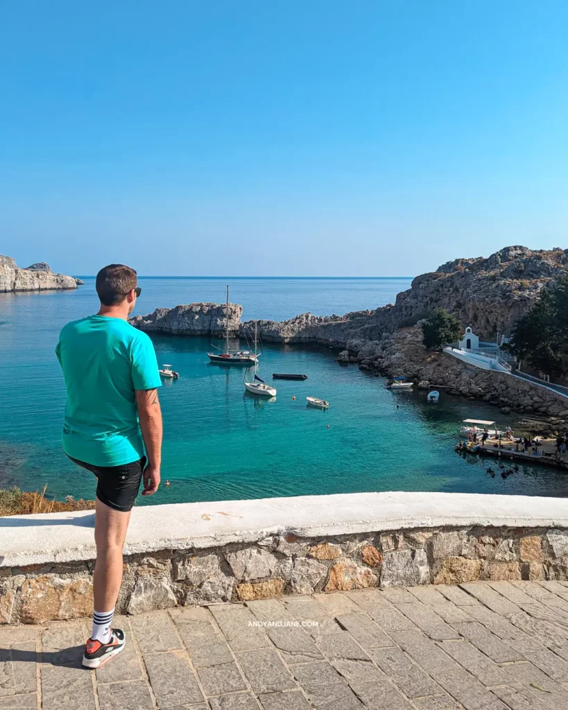 Andrew standing on a stone wall, gazing down at St.Paul's bay, the blue water & the boats below.