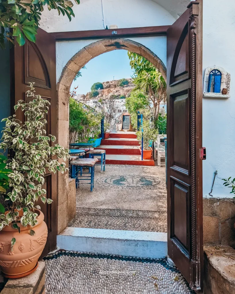 The mahogany open doors to Rainbird Cafe, looking out to the whitewashed village of Lindos in the distance.