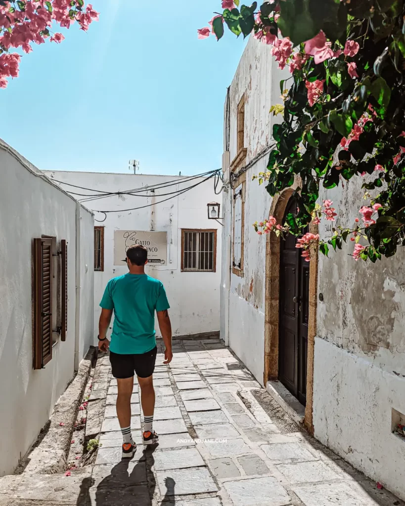 Andrew walking through a street in Lindos with pink flowers covering the walls of the houses.