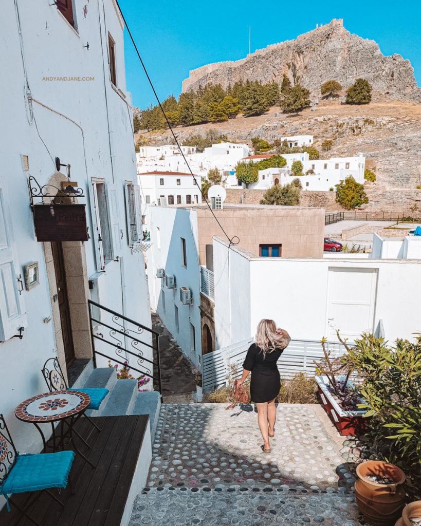 Jane walking down steps in the village of Lindos, with the Acropolis high up on the hill in the background.