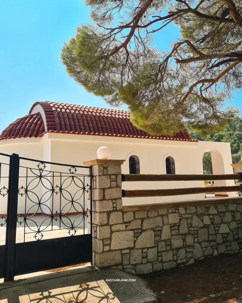 The cream chapel of Agio Nikolaos with a red roof & gates enclosing it.