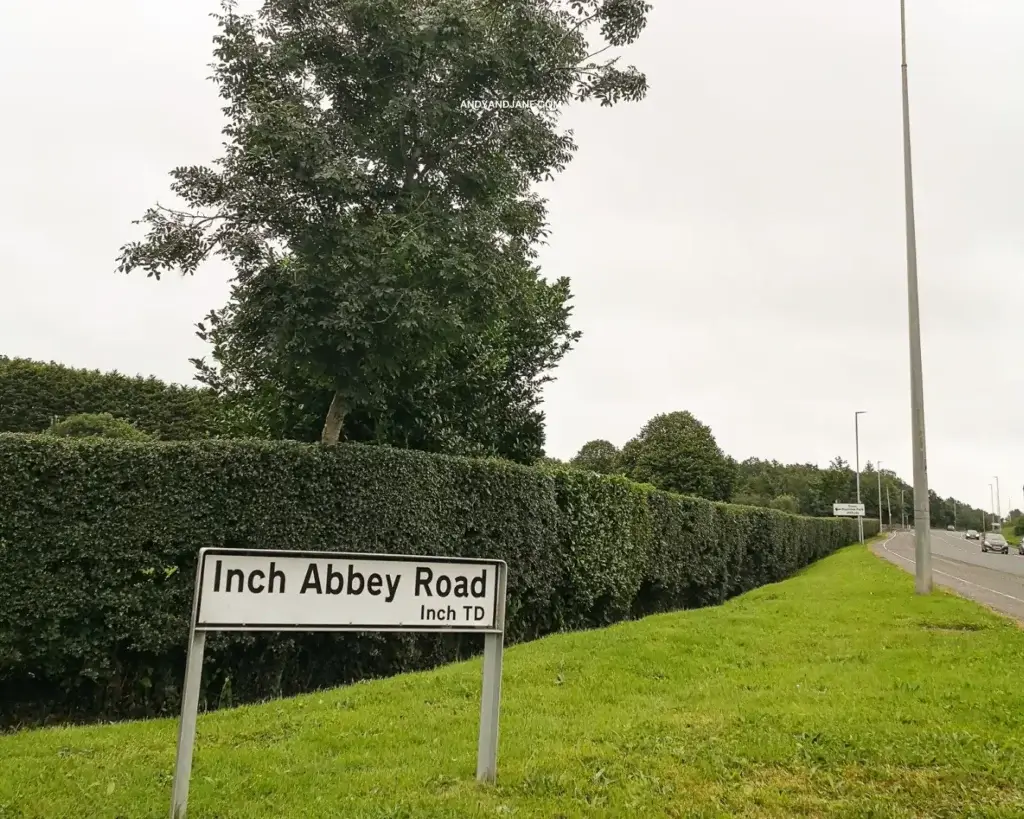 A road sign post in front of a hedge saying 'Inch Abbey Road'