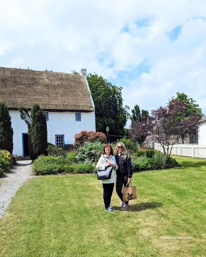 Jane and her mum standing in the green garden of the Lismacloskey Rectory. A beautiful white cottage with a thatched roof & colourful flowers out front.