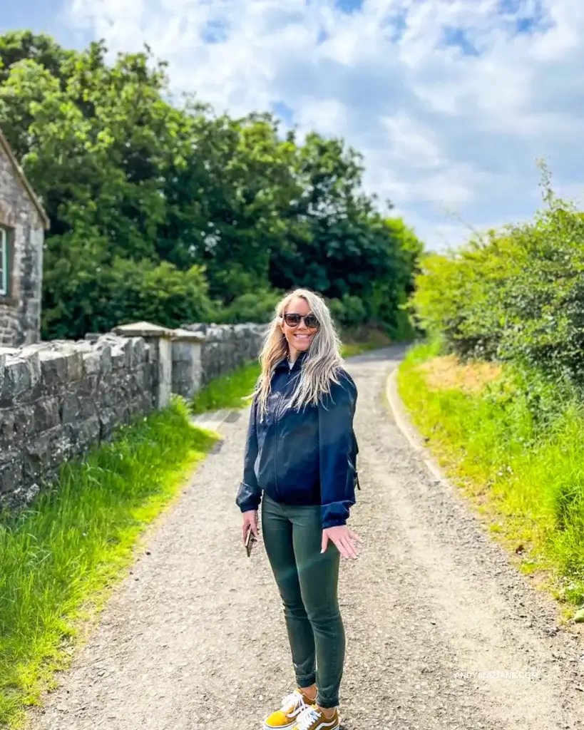 Jane standing in the middle of a country path at the museum, smiling to the camera.