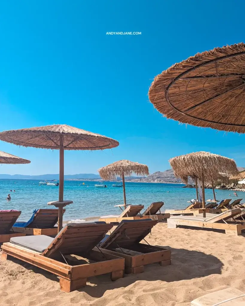 Pefkos Beach, with wooden sunbeds, umbrellas & crystal clear blue seas.