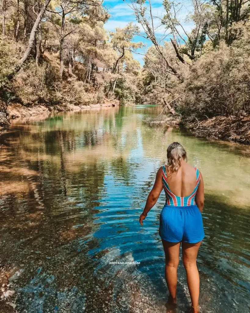 Jane with a stripe bathing suit on and blue shorts, wading in the water at Seven Springs. 