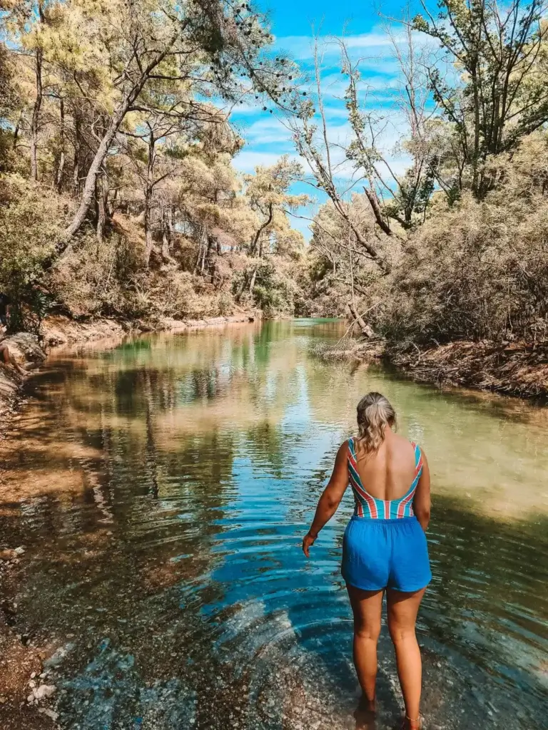 A girl with an orange & green striped bikini and blue shorts, taking a dip into the lake at Seven Springs.