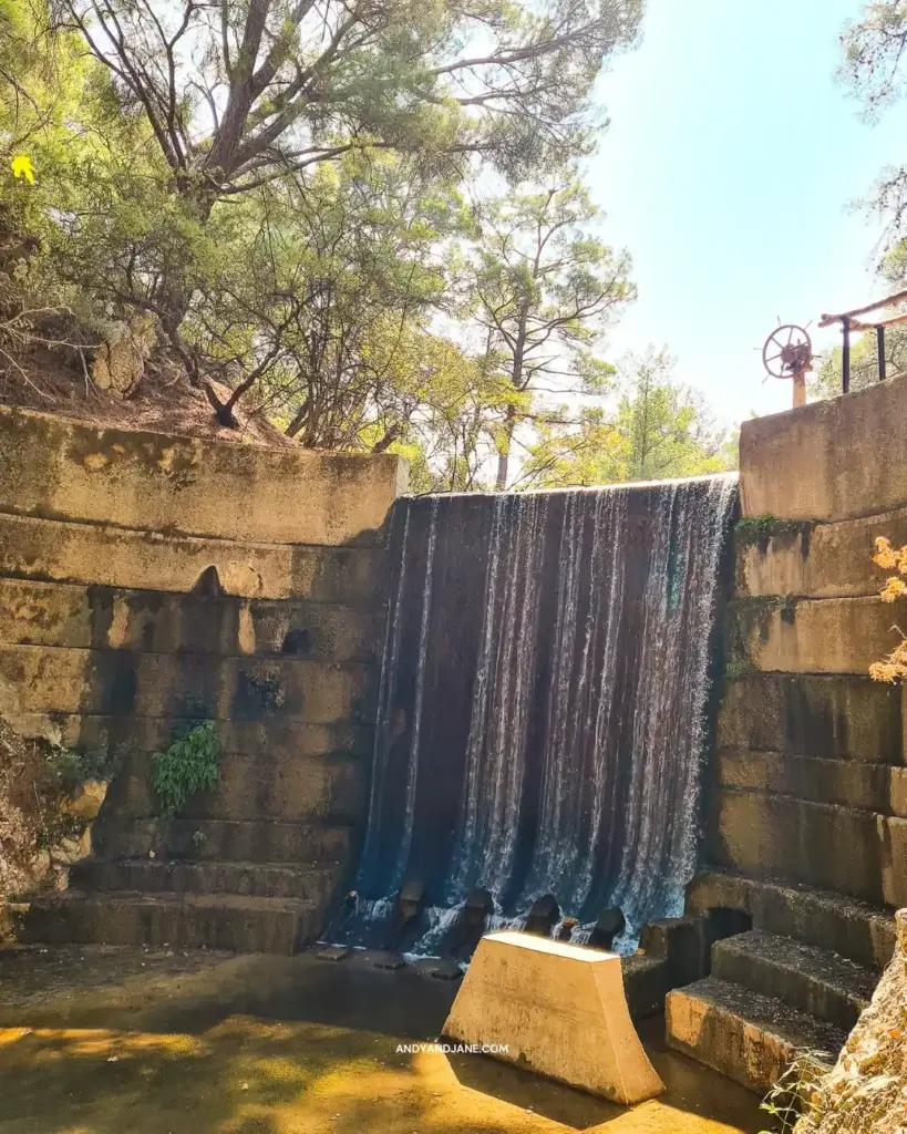 The waterfall & dam at Seven Springs with water flowing from it & trees surrounding it.