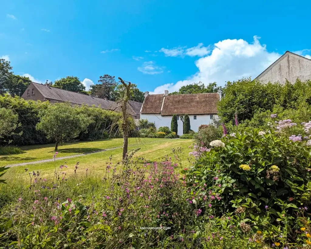 A beautiful garden with green grass & flowers, with a small white thatched cottage at the top. This is Lismacloskey Rectory. A pathway leads right up to the front door.