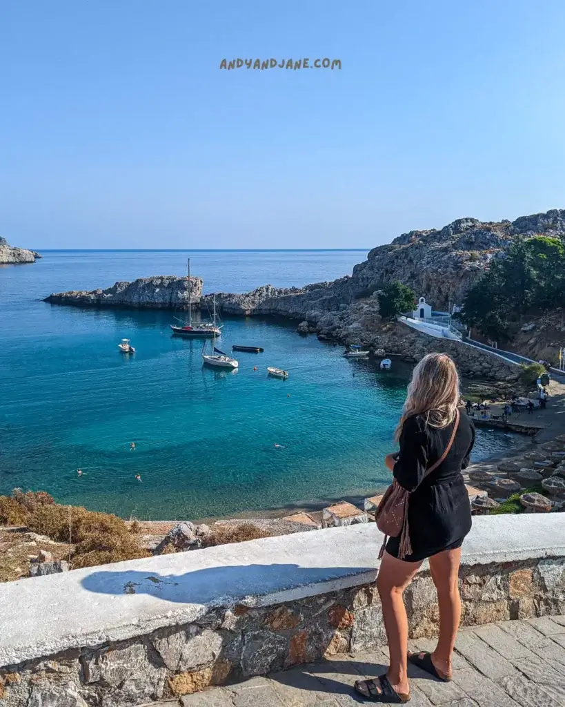 A woman standing in a black dress looking out over the crystal blue water and boats in the bay.