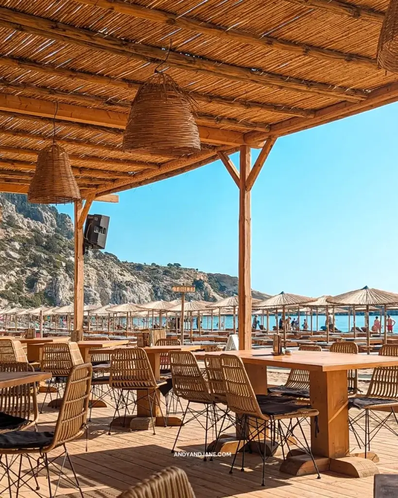 Chairs and tables at Ramal Beach Bar, overlooking Tsambika Beach. Bamboo lampshades hang from the ceiling.