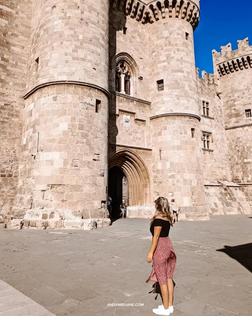 A girl in a black top & red skirt, standing in front of a huge castle with turrets in Rhodes.