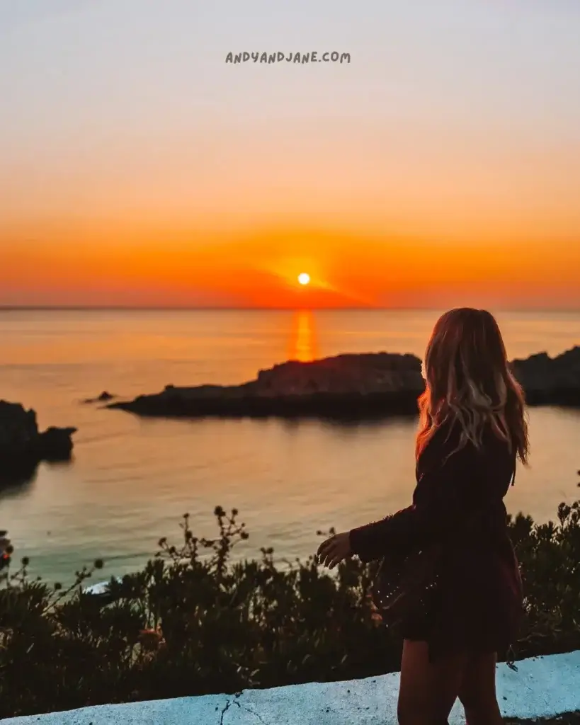 A girl looking out across the water towards the sun coming up in the distance.