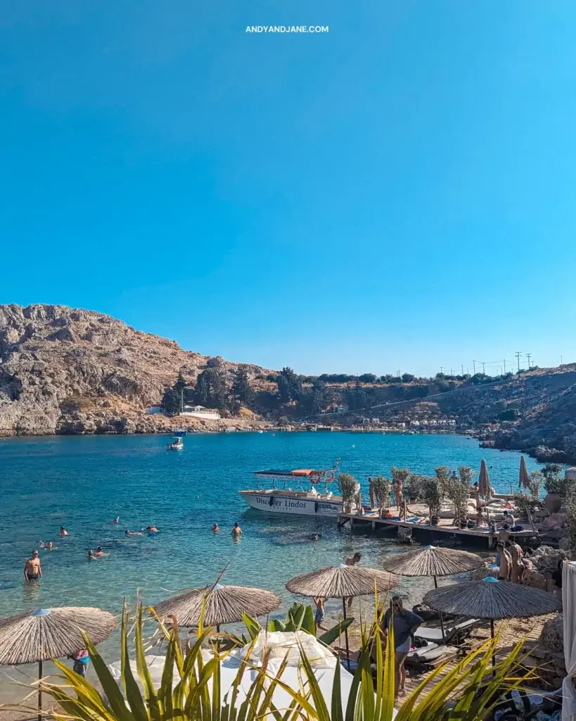 Looking out over the bay towards a boat called 'Discover Lindos' & people enjoying the water.