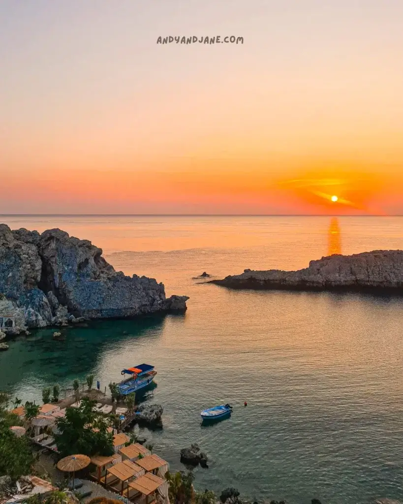 Overlooking St. Paul's Bay with two boats in the water at sunrise. The sky is lit up orange and yellow.