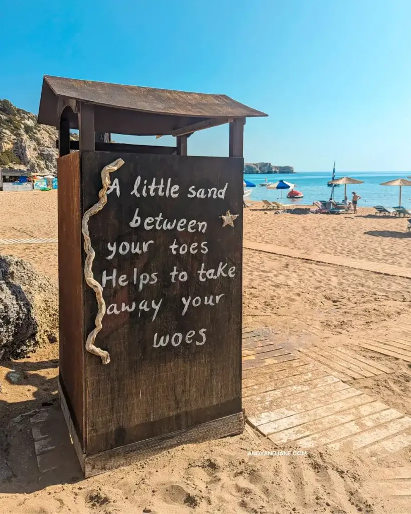 A wooden hut at Tsambika Beach with the phrase 'A little sand between your toes helps to take away your woes' engraved on it.