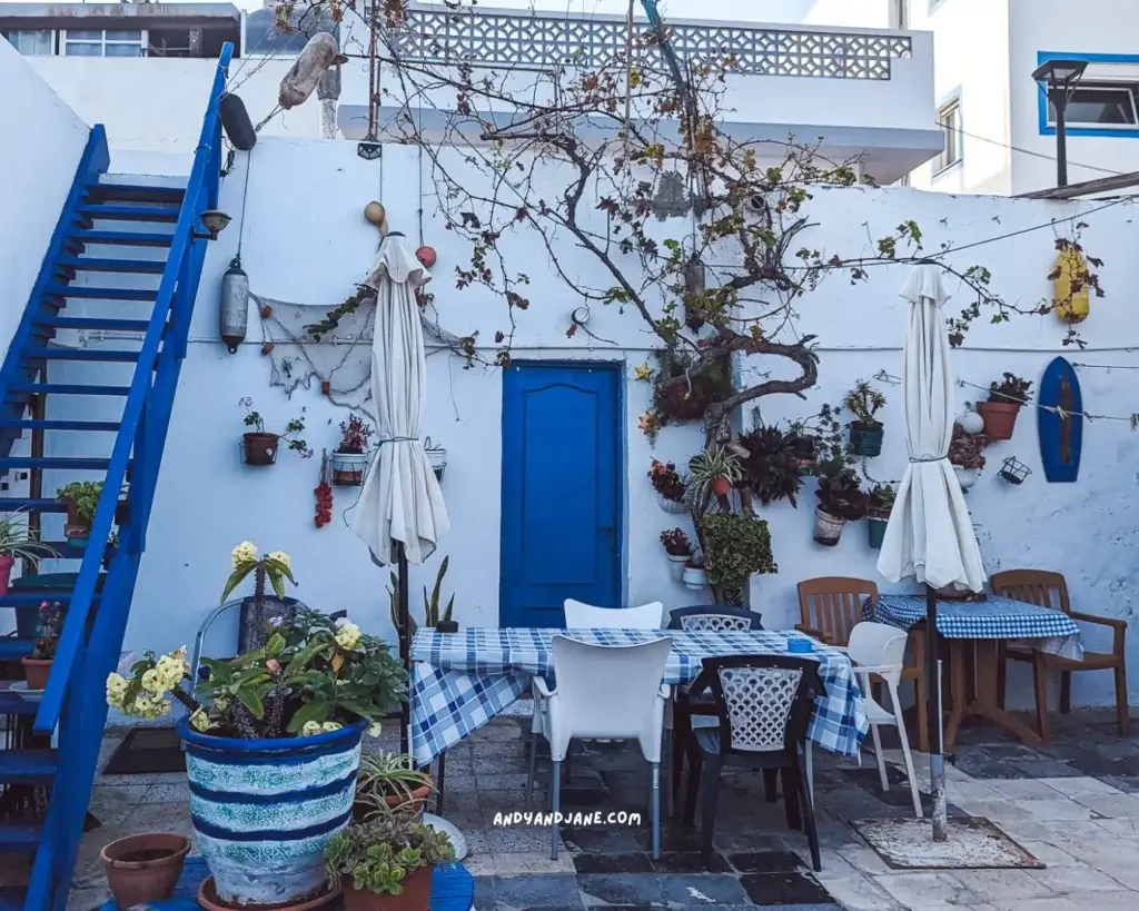 A terrace of a fish restaurant in Corrlaejo with blue stairs, a blue door & flower pots hanging on the wall.