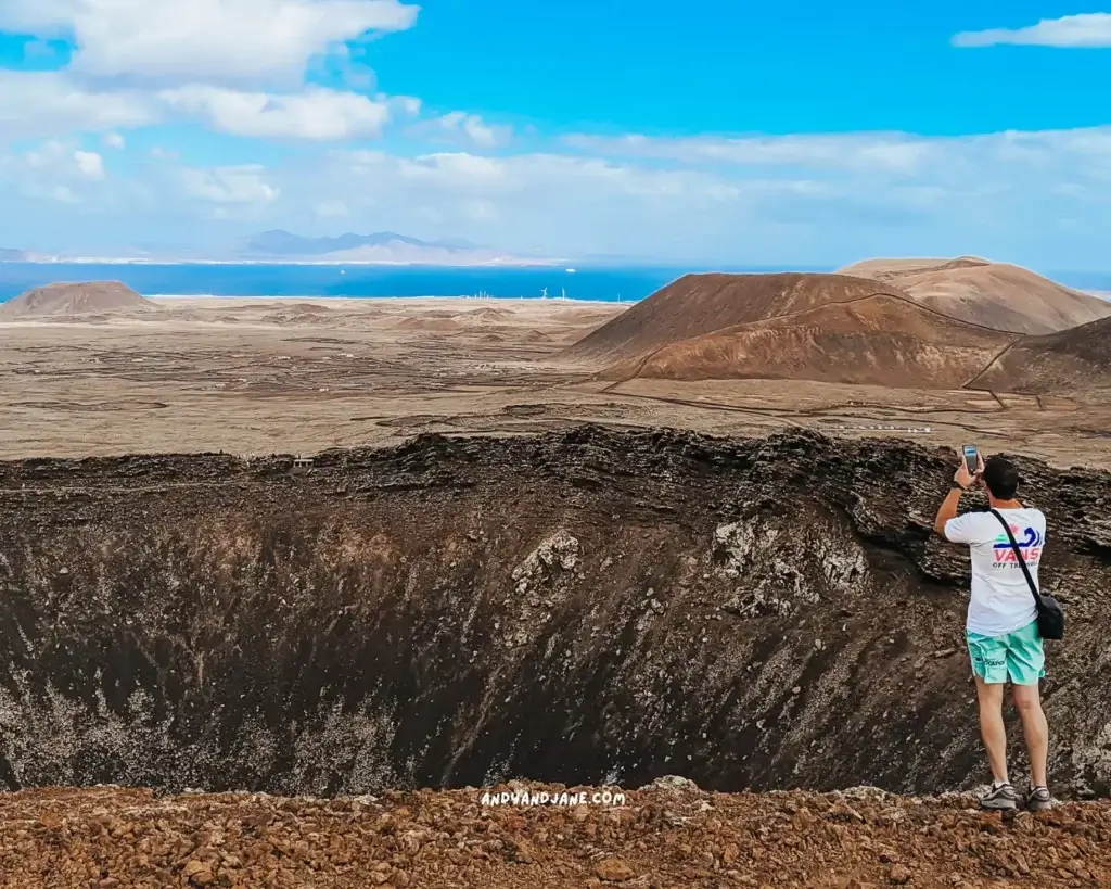 A man taking a picture of the ocean views on top of a volcano crater in Fuerteventura.