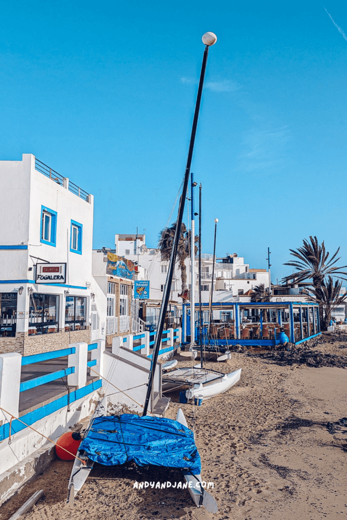 A sailboat sitting on a beach in front of the restaurants in Corralejo.