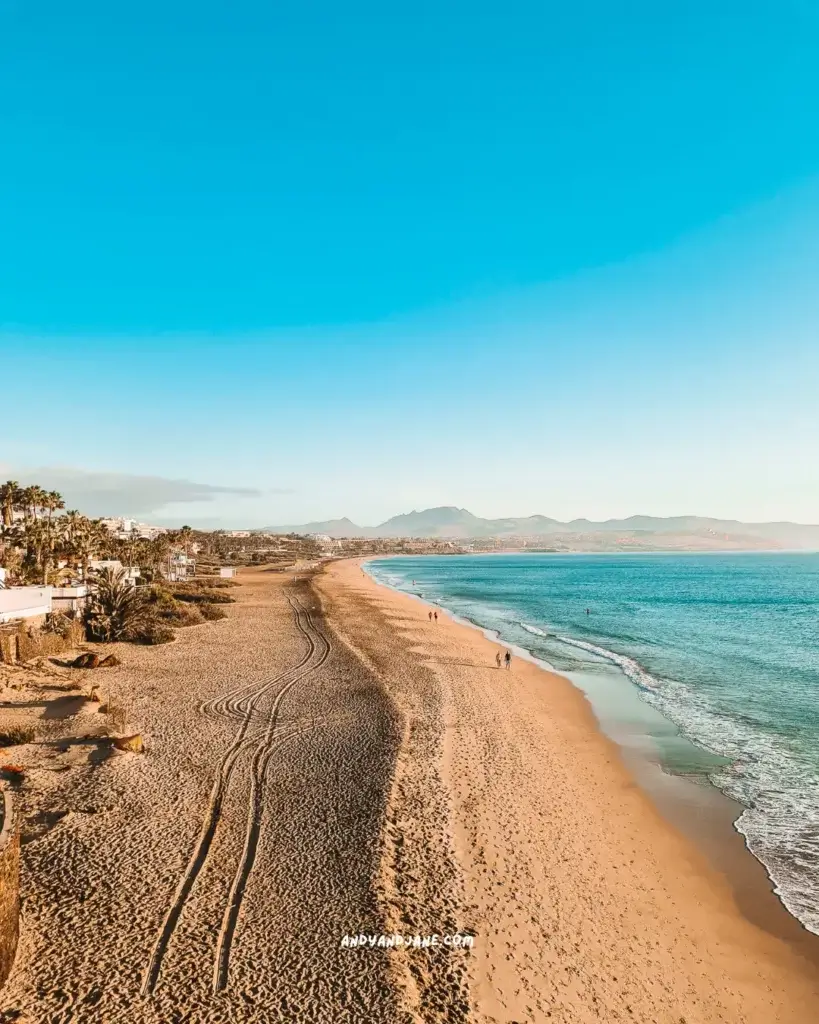 A long golden sandy beach in Costa Calma with the blue waves lapping the sand.