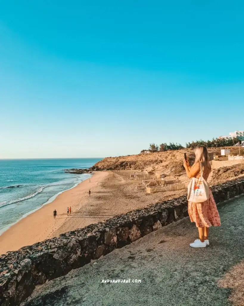 A woman taking a picture of the ocean from above a beach in Costa Calma.