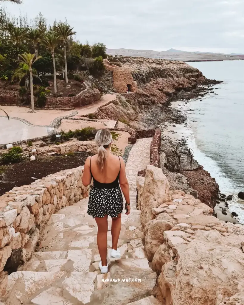 A woman walking down rock steps towards the ocean and a viewpoint.