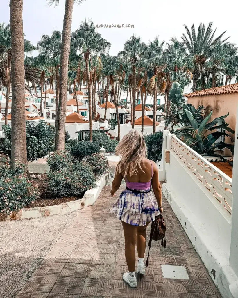 A woman walks down a scenic path in Costa Calma surrounded by lush palm trees, embracing the beauty of nature.