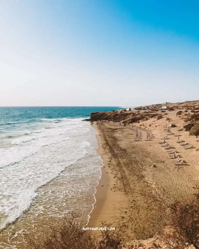 A golden sandy beach in Costa Calma with the waves lapping the shore & sunbeds covering parts of the sand.