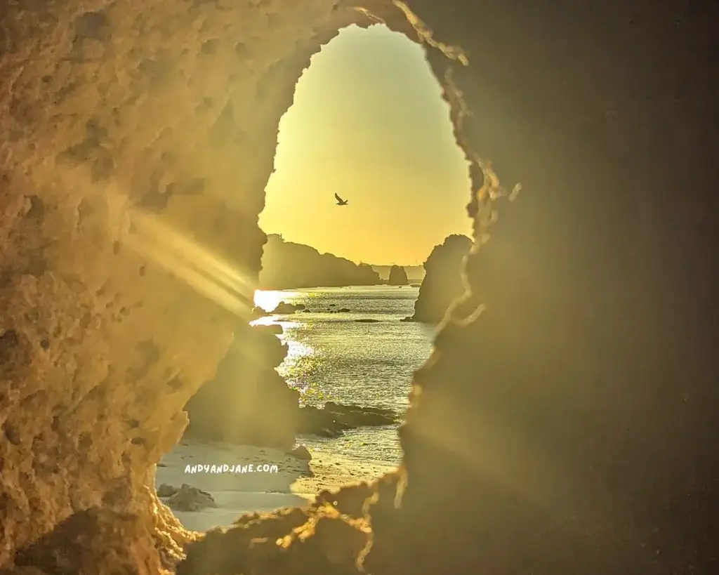 A bird flying over the ocean through a hole in a rock.