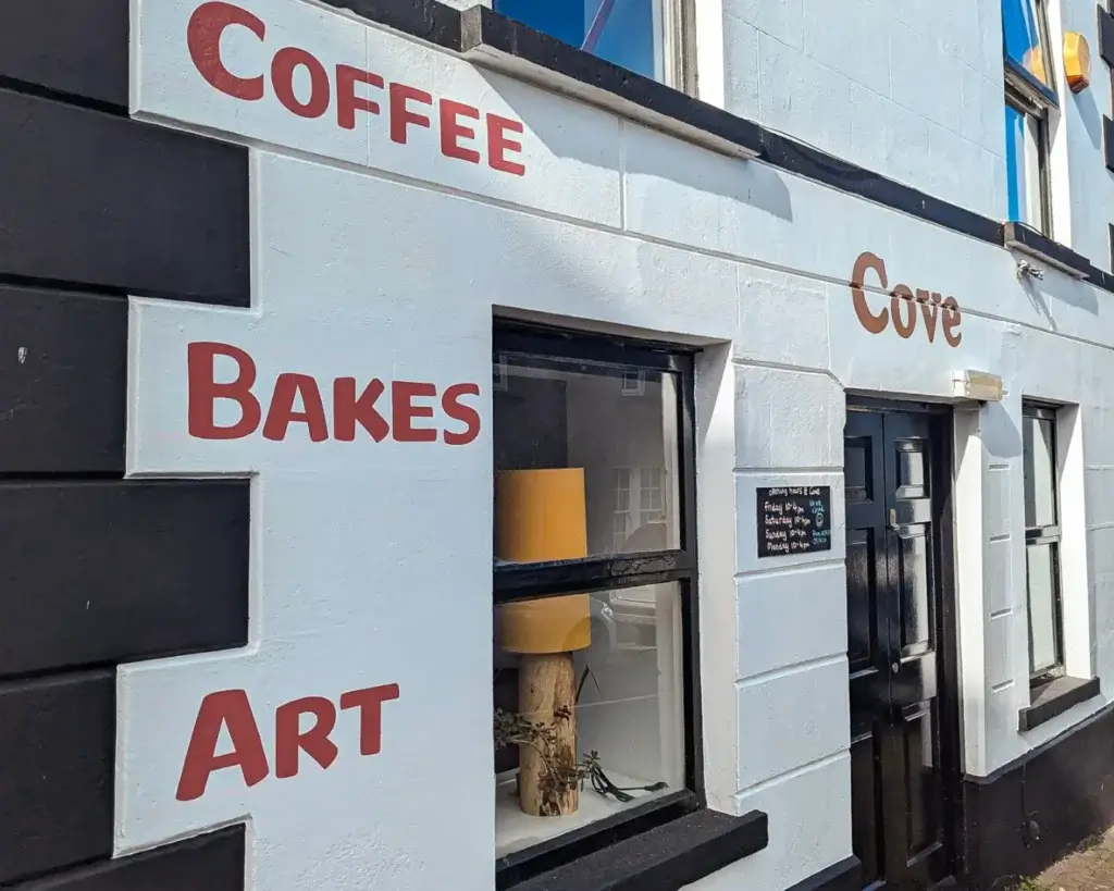 Exterior of a quaint cafe with "COFFEE BAKES ART" painted on its white and black facade.