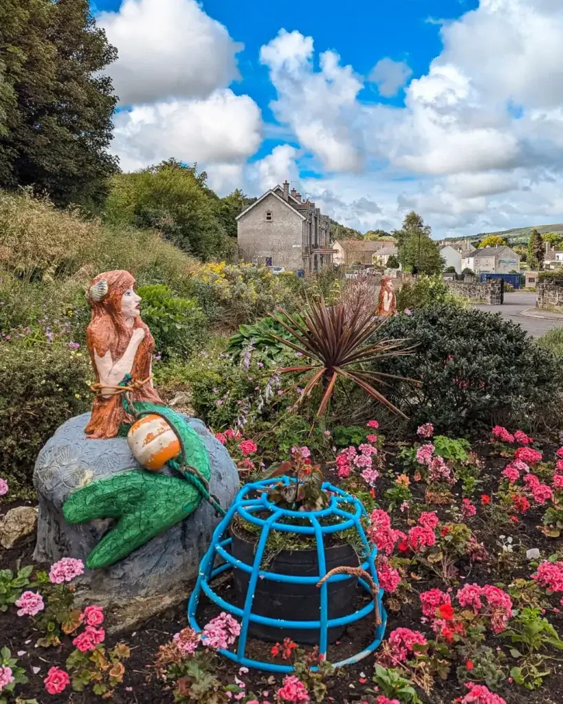 Vivid garden with mermaid statues, flowers, and blue sky.