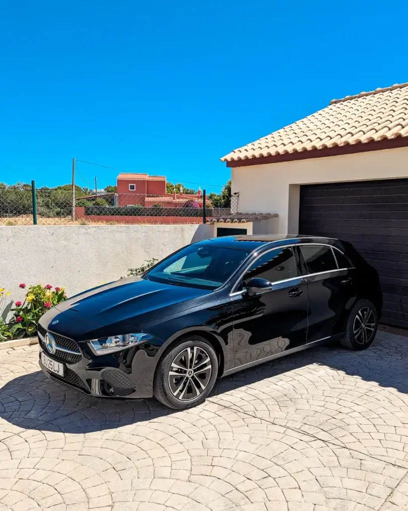 A black Mercedes car sitting in a driveway in front of a garage.