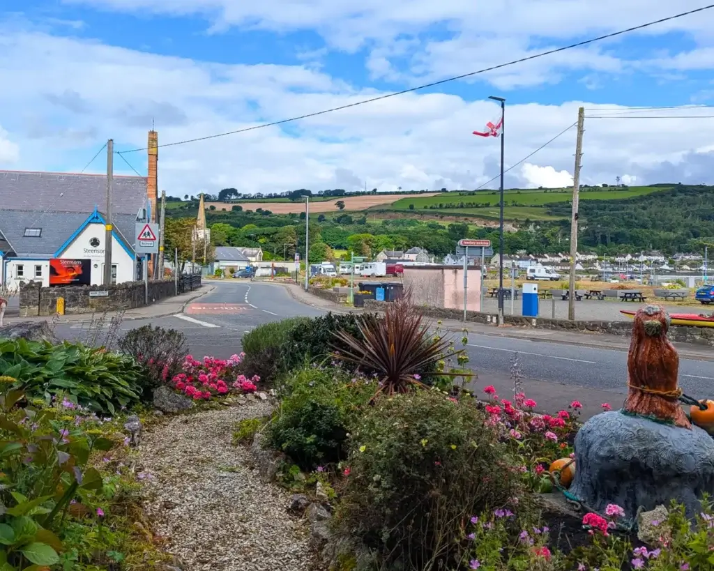 A scenic view of a coastal village with colorful flowers and rolling hills in the background.