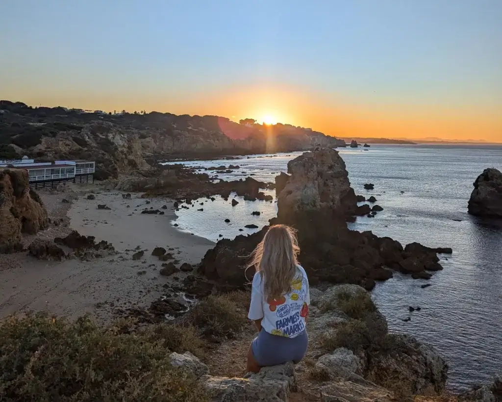 woman sitting on a cliff overlooking Praia dos Arrifes beach