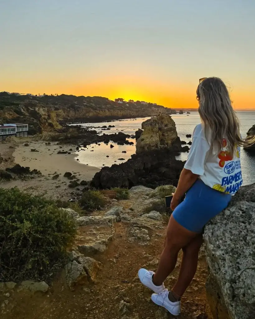 a woman sitting on a rock looking out at the ocean