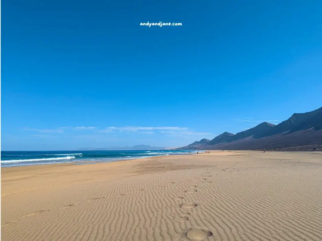 The sandy beach of Cofete, with waves, mountain backdrop under a clear blue sky