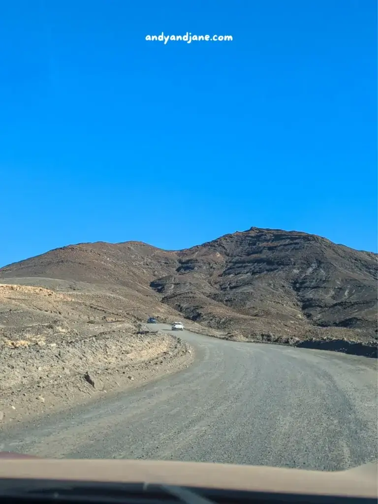 A curvy road winding through a barren, mountainous landscape with a clear blue sky overhead.