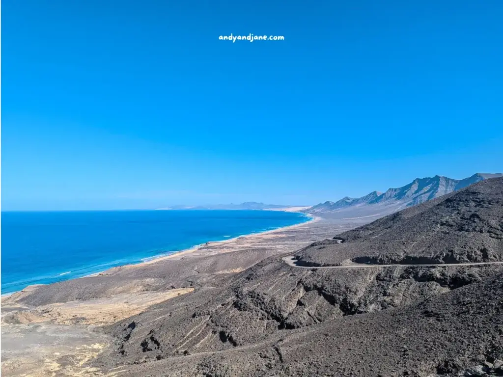 Coastal road curving along a desert landscape with mountains and a clear blue sea at Playa de Cofete in Fuerteventura.