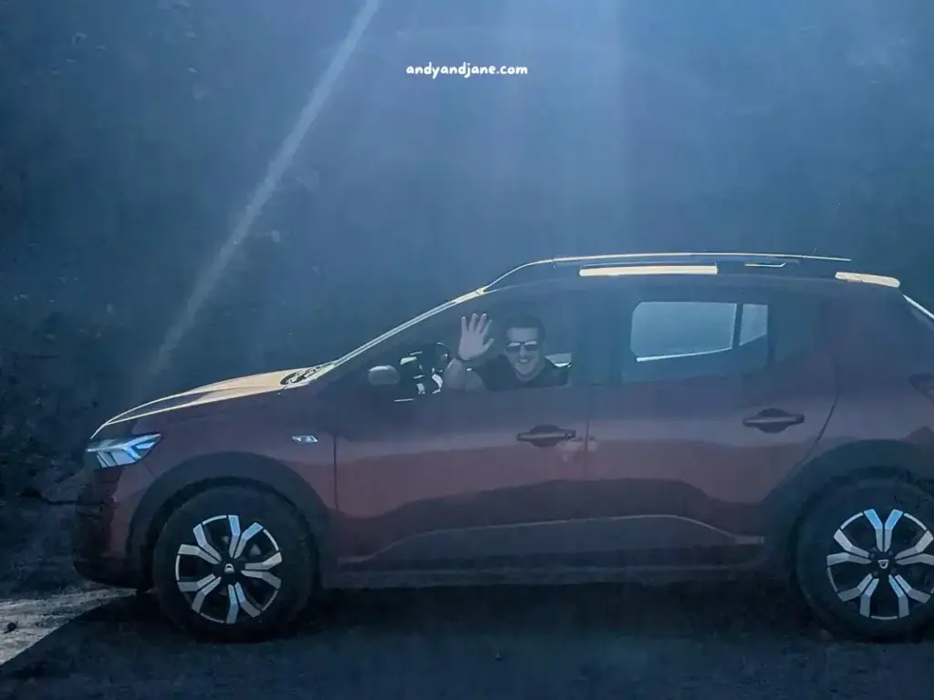 A red car with sunrays shining down, and a person waving from inside.