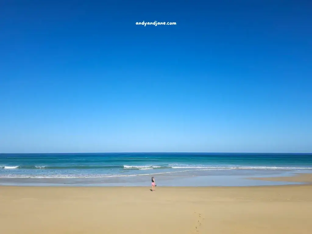 A person standing in front of water at Cofete Beach with blue sky and clear horizon.