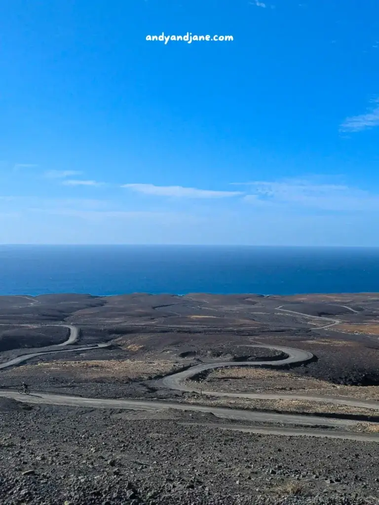 Winding road through a barren landscape with ocean horizon under a clear blue sky. 