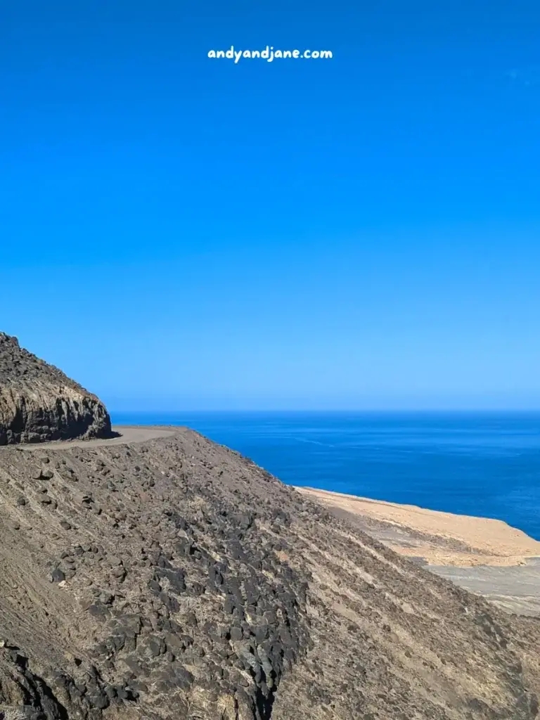 Rocky mountain slope with ocean horizon under a clear blue sky.