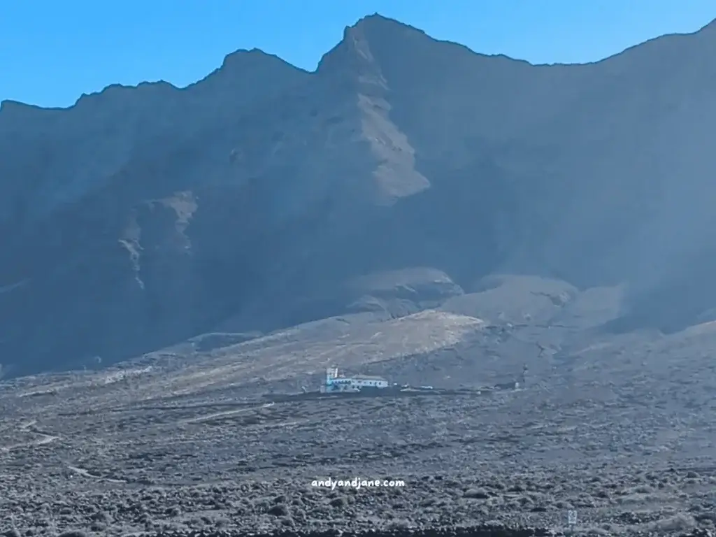 A remote building at the base of a rugged mountain under a clear blue sky.